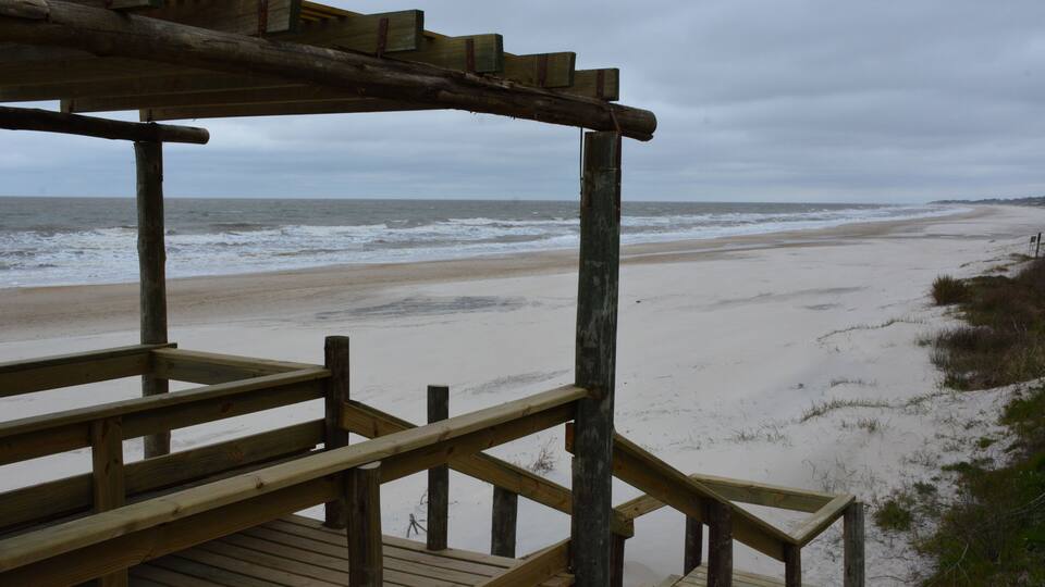 A wooden pier leading to a beach with a cloudy sky.