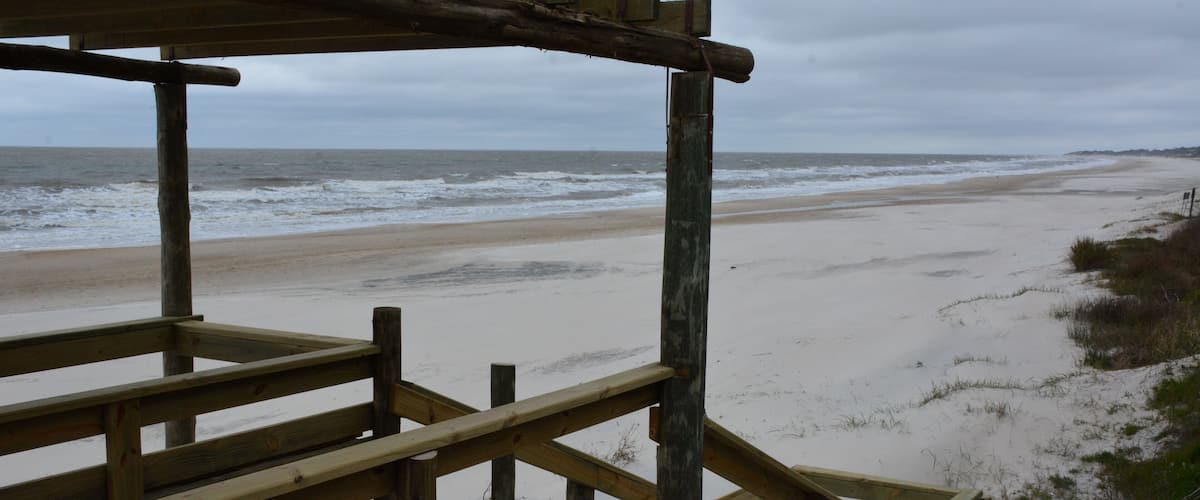 A wooden pier leading to a beach with a cloudy sky.