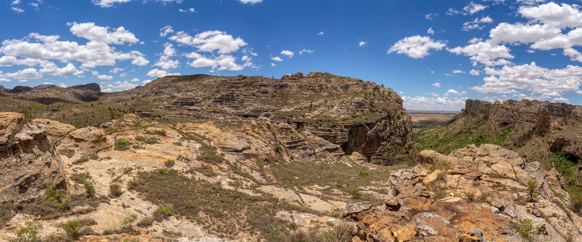 A rugged mountainous landscape with layered rock formations and sparse vegetation under a clear blue sky.