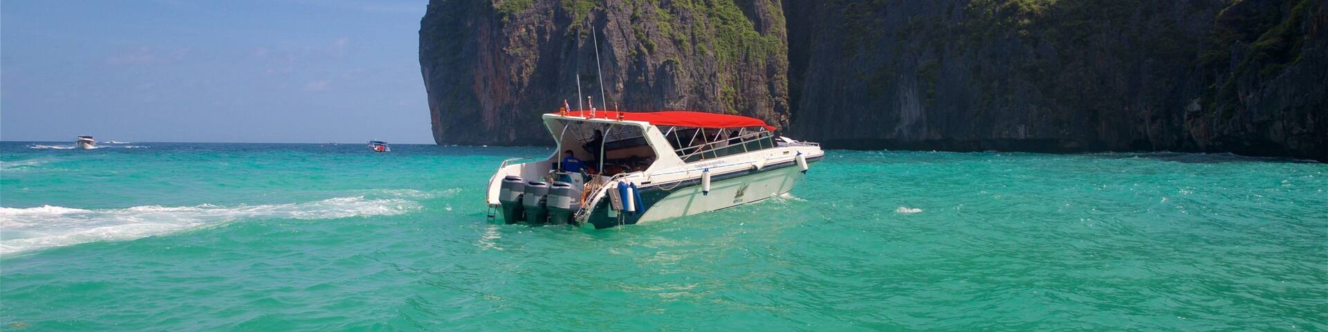 A boat with a red canopy sailing on turquoise waters, surrounded by large limestone cliffs.