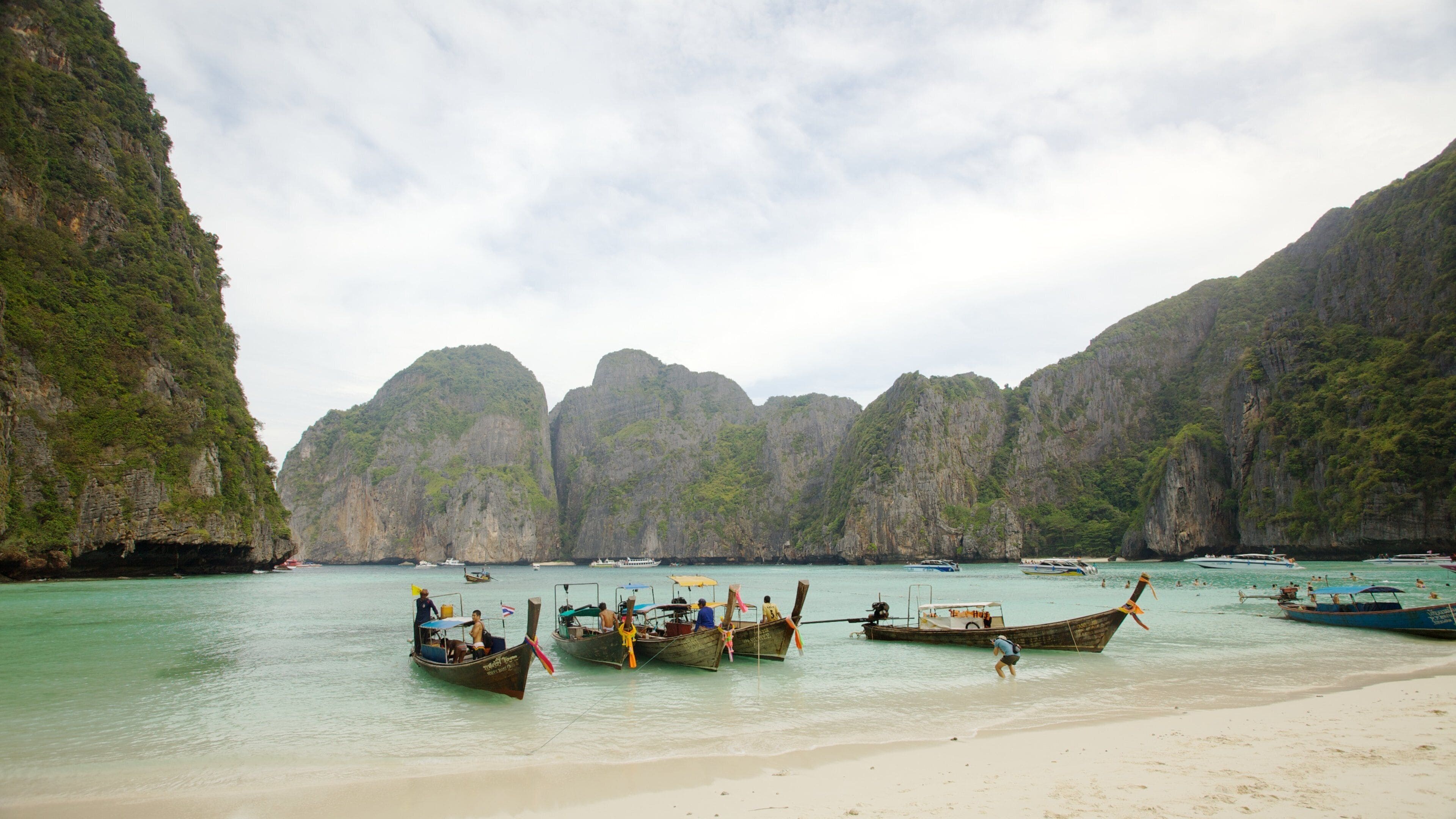 A beach with boats and rocky cliffs.