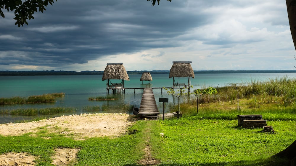 Hammocks on dock along the lake shore with dark blue cloudscape, El Remate, Peten, Guatemala