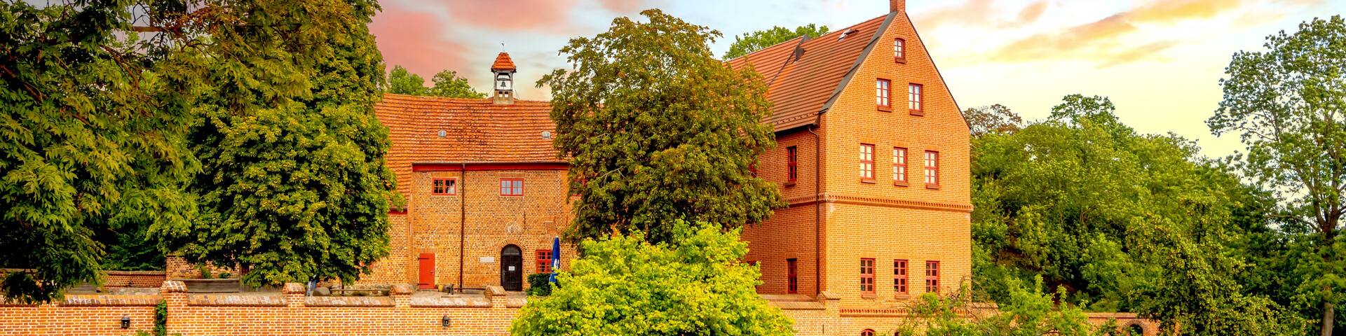 A large brick building with a clock tower, surrounded by trees and a grassy area.
