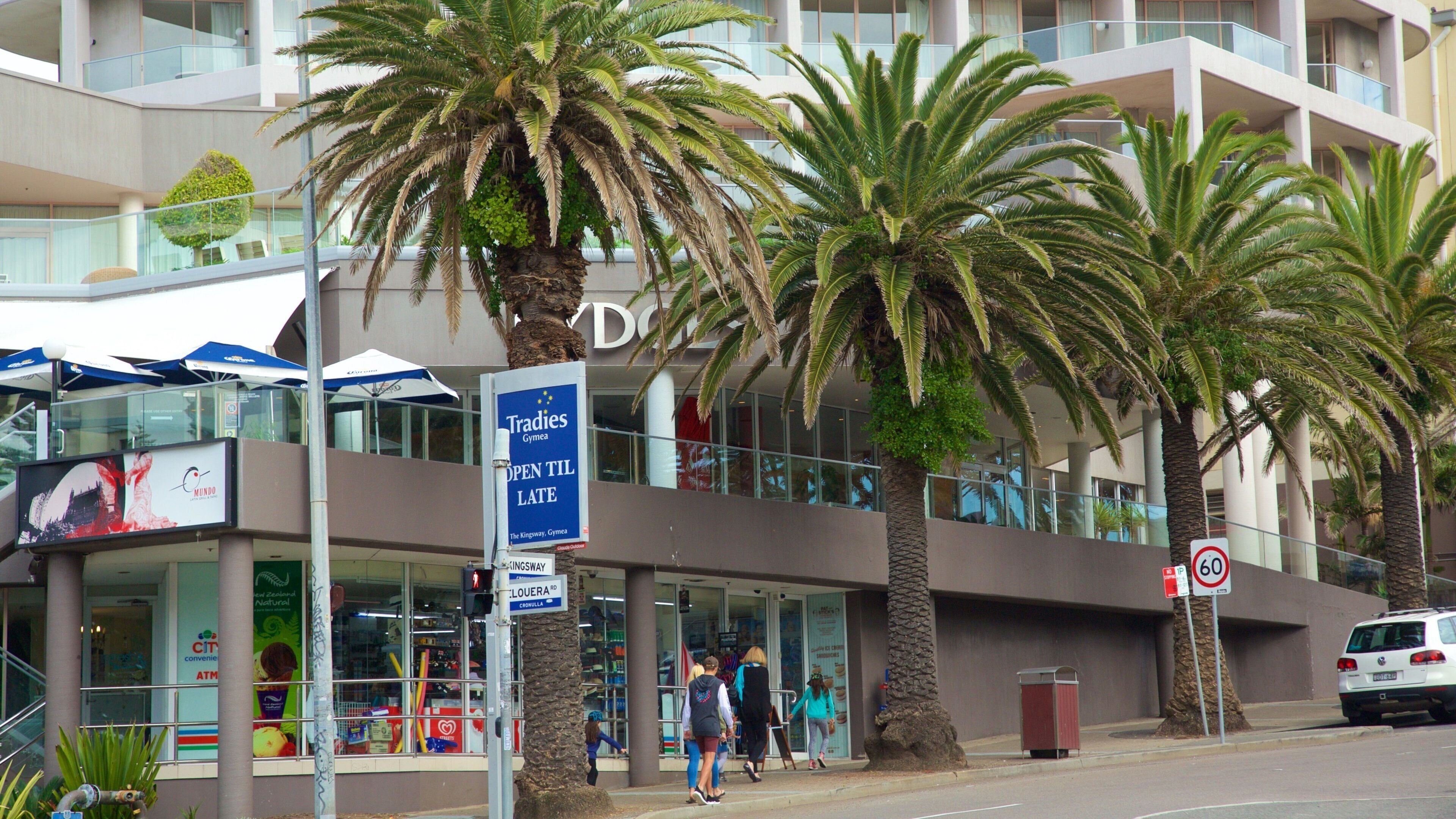 Un edificio moderno con palmeras frente a él. Hay un letrero que dice 'Tradies Gym' y una señal de límite de velocidad de '60'.