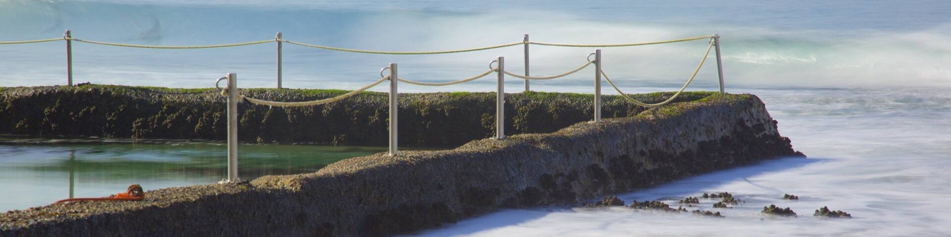A rocky breakwater with a rope barrier, calm sea, and distant shoreline.