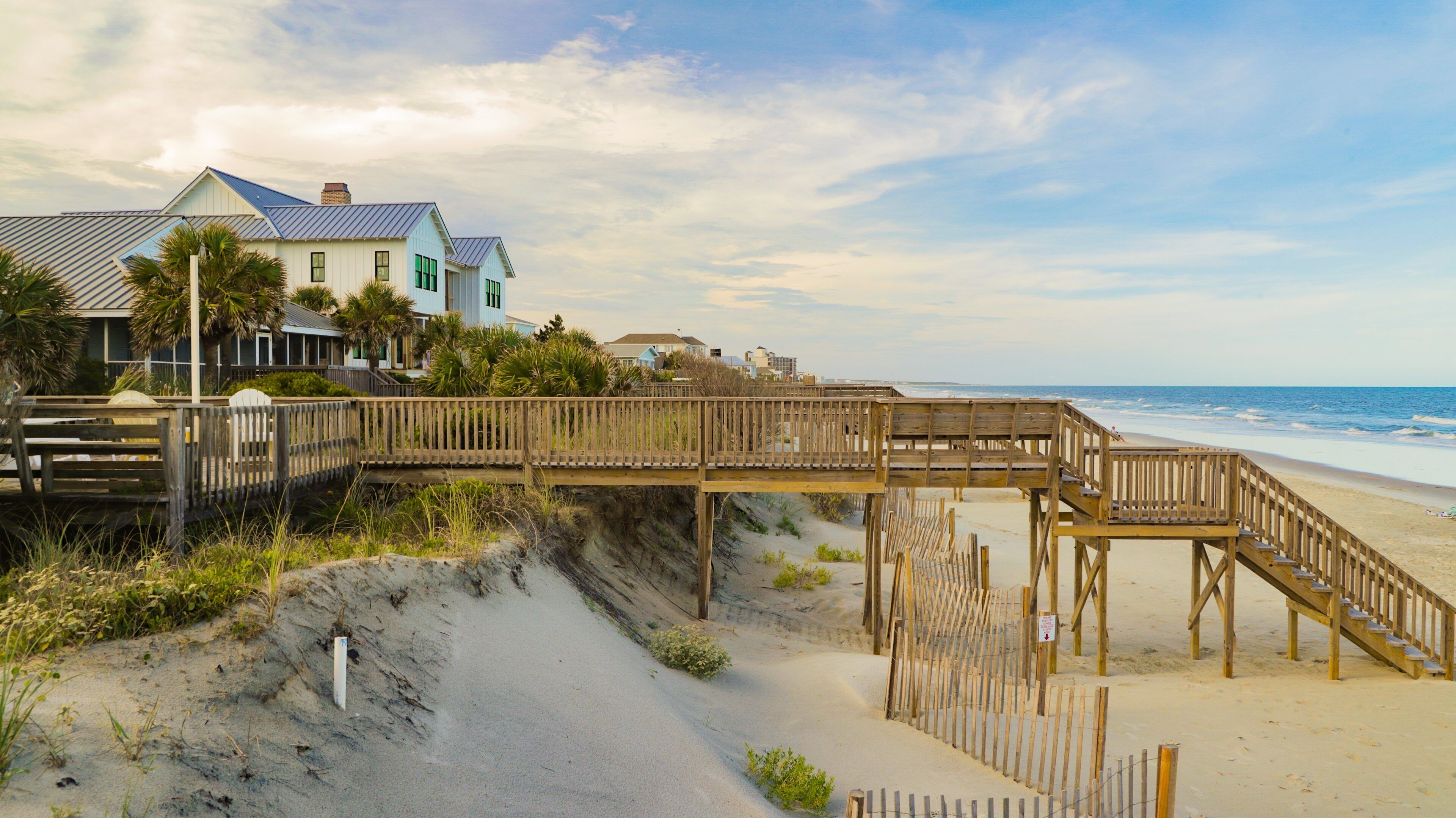 A wooden boardwalk leading to a beach with a house in the background.