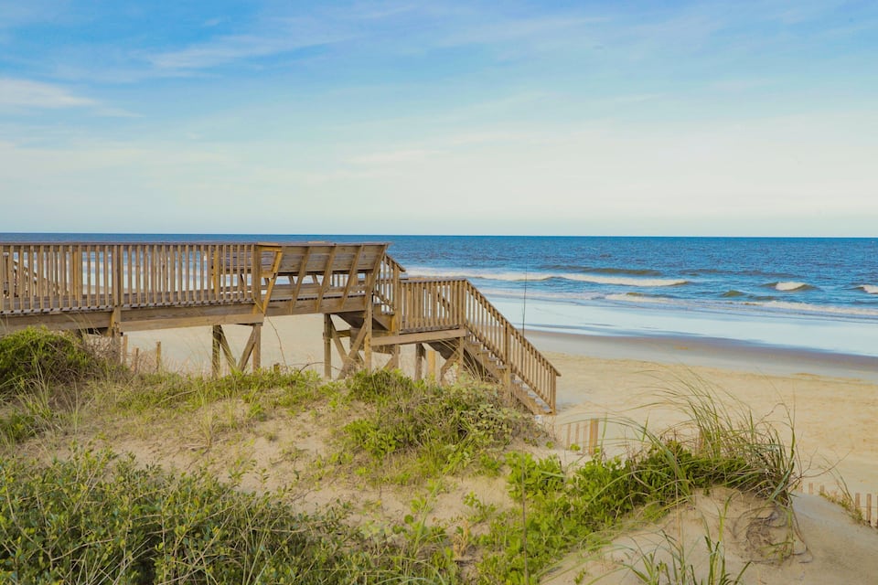 A wooden boardwalk leading to a beach with waves in the background.