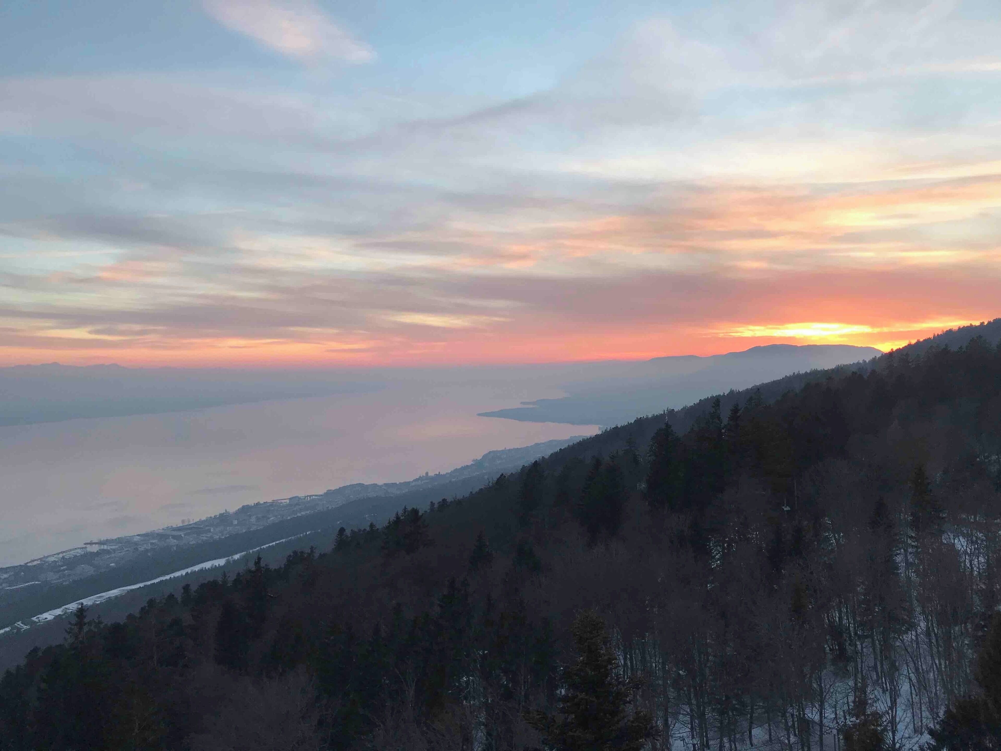 A mountainous landscape with a sunset over a body of water.