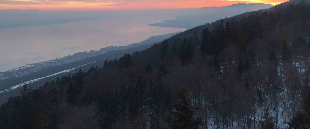 A mountainous landscape with a sunset over a body of water.