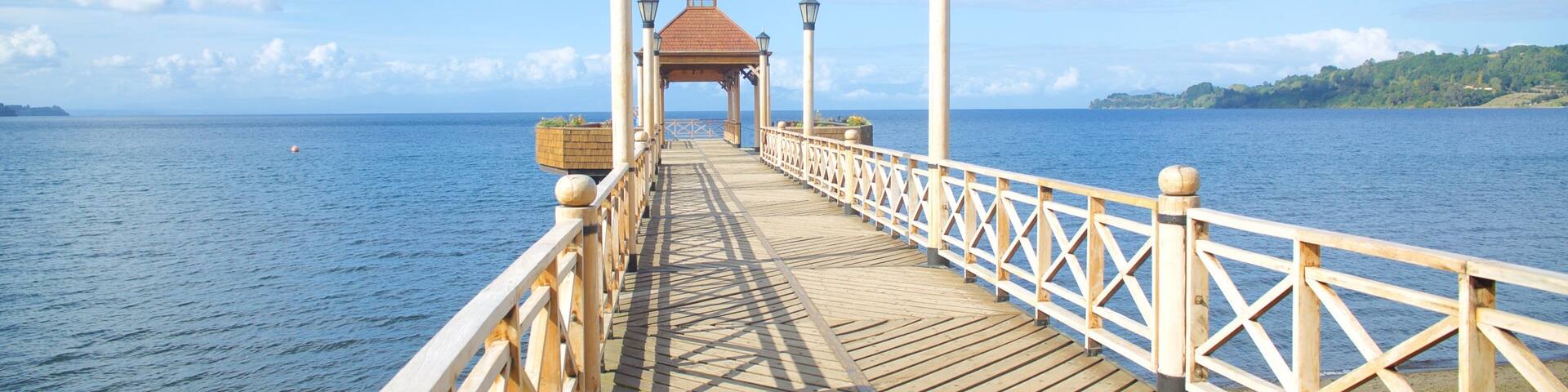A wooden pier extending into a calm sea, with a gazebo and lanterns at the end.