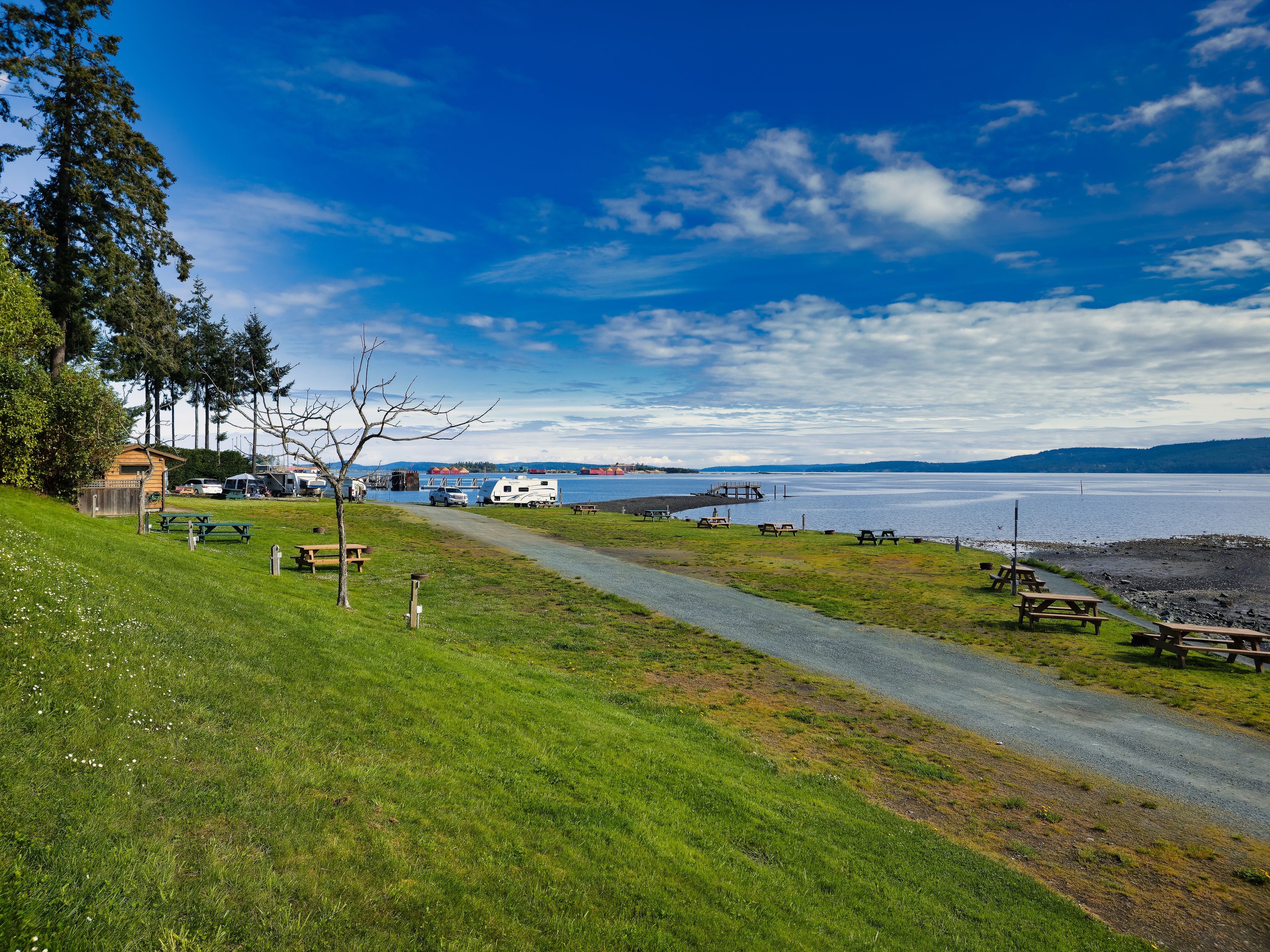 A lakeside campsite with picnic tables, RVs, and a wooden cabin.
