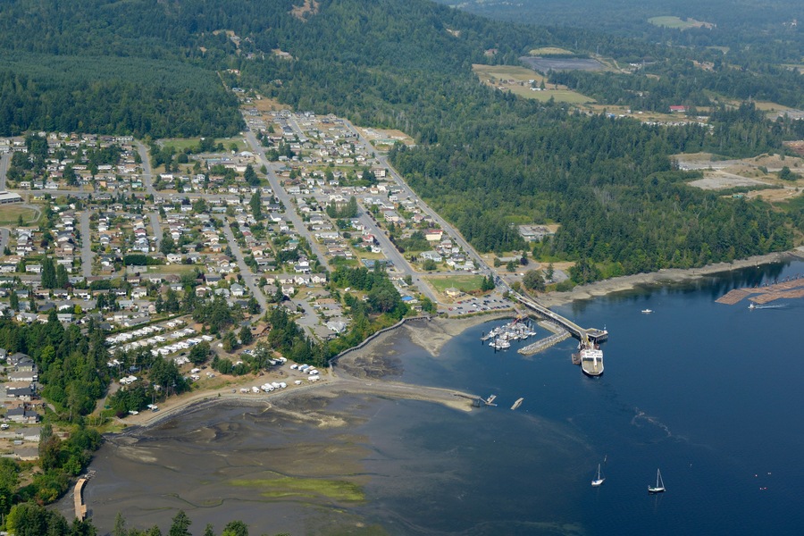 An aerial view of a coastal town with residential areas, a marina, and a bridge connecting the land to the water.