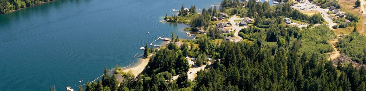 Ein See, umgeben von dichten Wäldern und einer kleinen Stadt mit sichtbaren Gebäuden und Anlegestellen.
