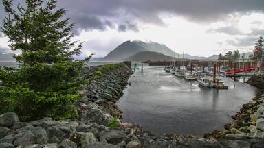 Kelsey Bay - north shore of Vancouver Island, BC. The view on the harbour, boats, rocks, pine tree, pier and mountains in the background. Stormy dark sky.