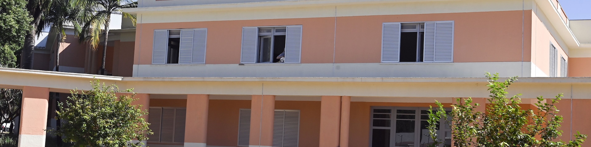 Un edificio de dos pisos con techo plano, ventanas grandes con contraventanas y un camino de entrada pavimentado.