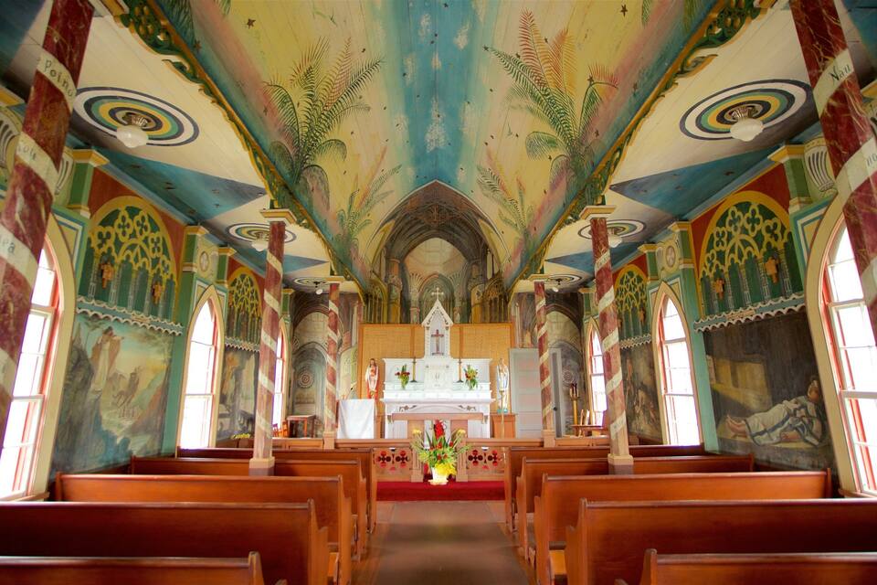 Ein Kircheninneres mit Holzbänken, einem zentralen Altar und farbenfrohen Fresken an der Decke.