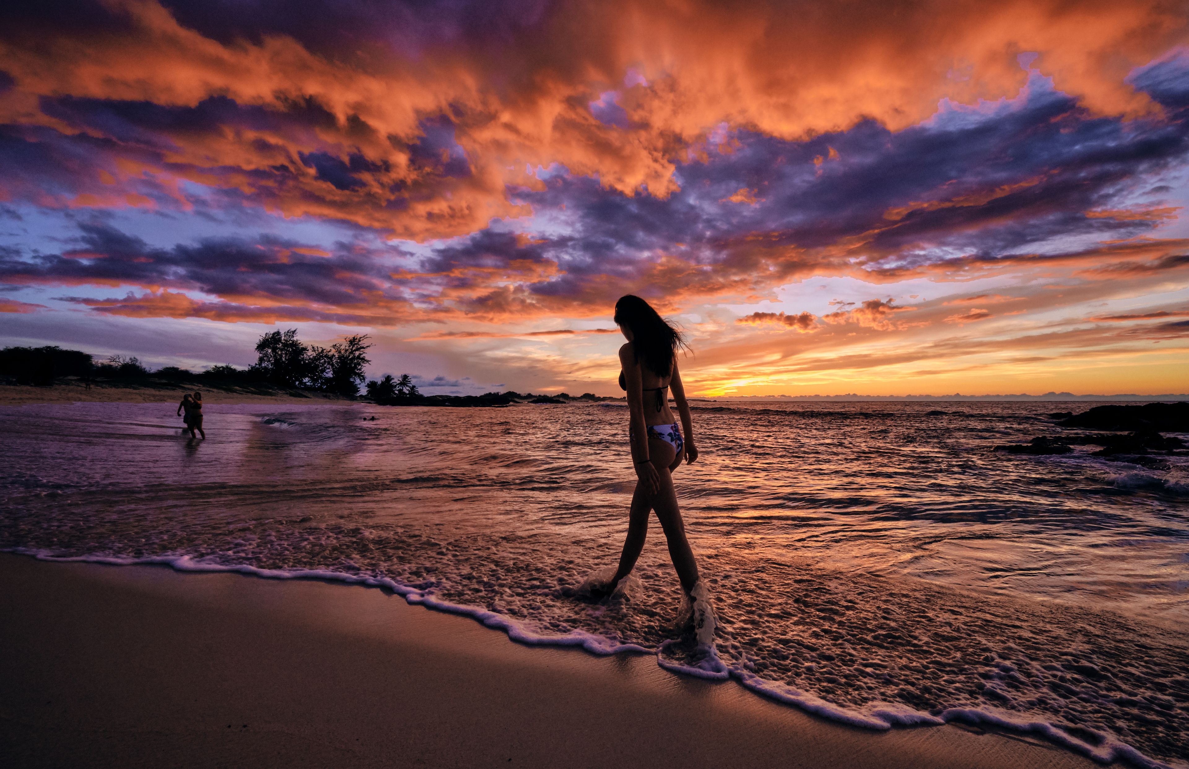 Une plage au coucher du soleil, où une femme se promène le long du rivage.