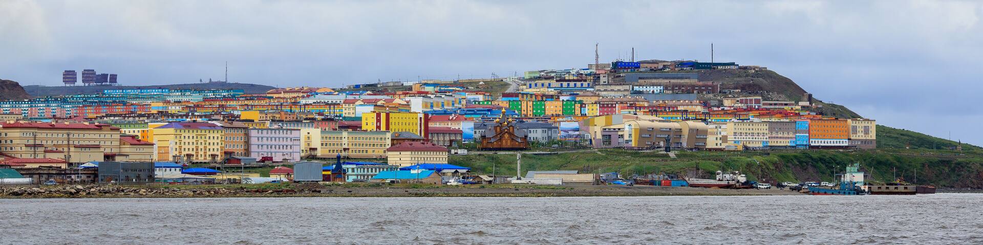 A coastal city with colorful buildings and a hill in the background.