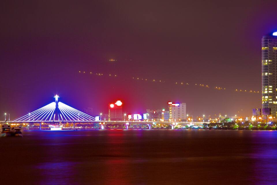 A city skyline at night with illuminated buildings and a bridge with blue lights.