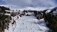 Une piste de ski enneigée, avec des remontées mécaniques, des arbres et une montagne en arrière-plan.