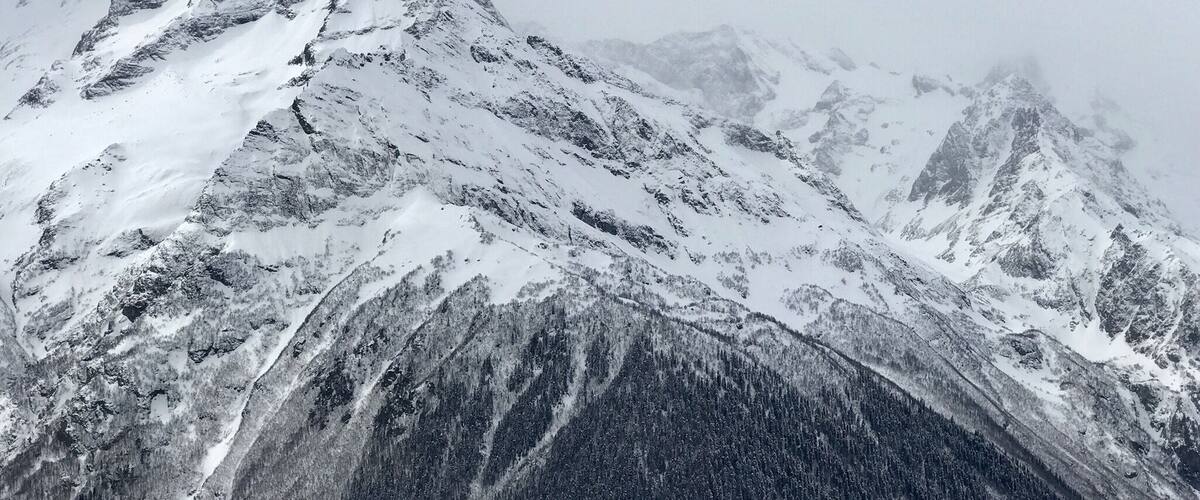 Un pico montañoso cubierto de nieve, con terreno accidentado y laderas boscosas.