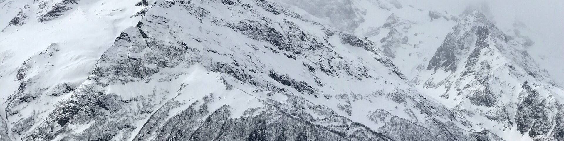 A snow-covered mountain peak with rugged terrain and forested slopes.