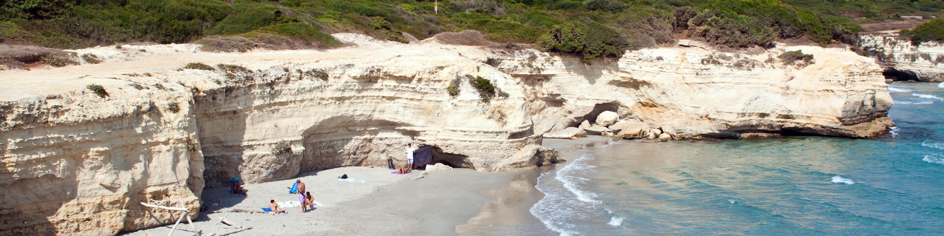 Uma praia costeira com águas turquesa cristalinas, areal arenoso e falésias rochosas.