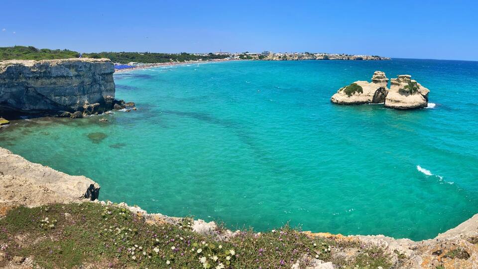 A coastal landscape with a prominent cliff, clear turquoise waters, and rocky formations.