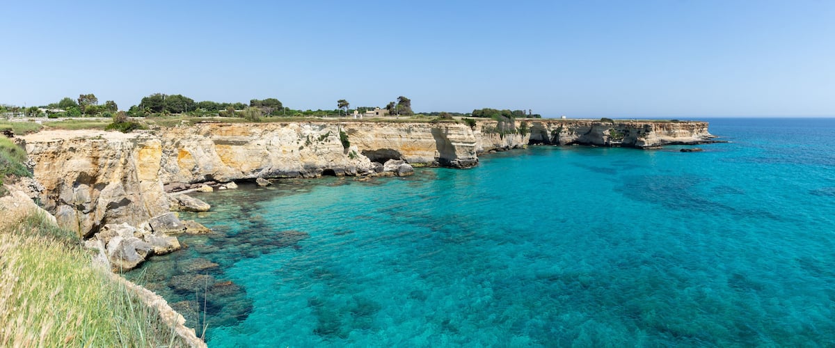 A coastal cliff with clear turquoise waters and a distant shoreline.