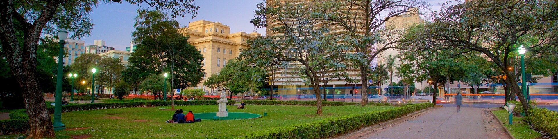 Um parque com um edifício curvo, árvores e um caminho pavimentado.