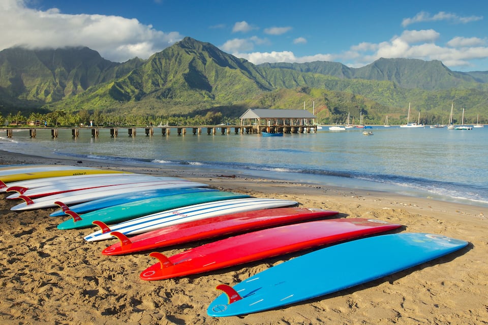 Una spiaggia con tavole da surf colorate allineate e una montagna sullo sfondo.