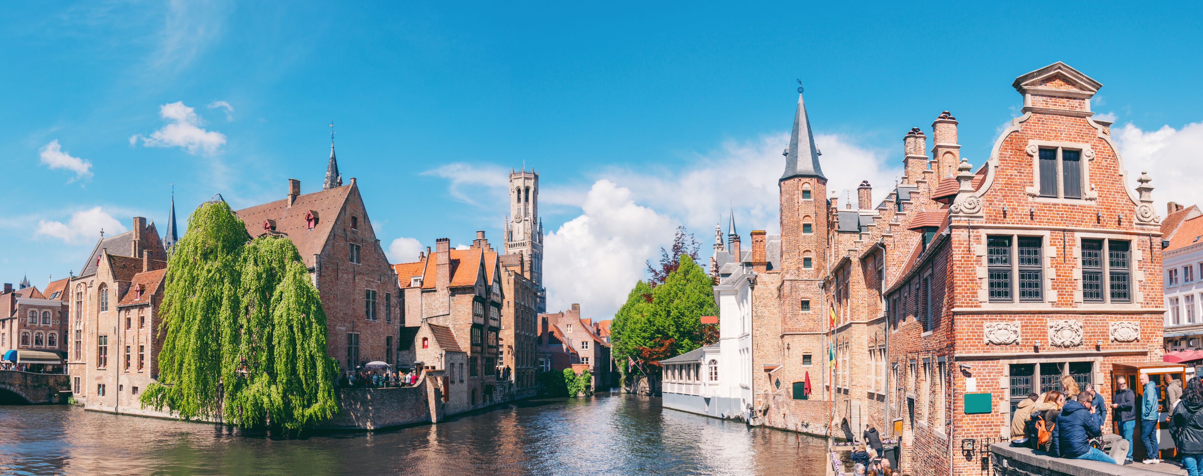 Un canal bordé de bâtiments historiques, une haute tour et un bateau.
