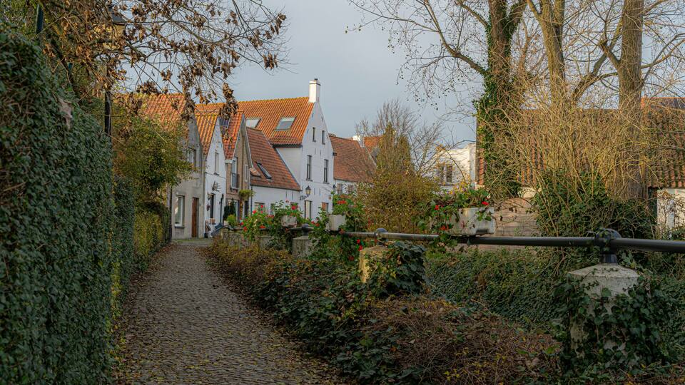 A cobblestone path leading to a traditional building with a red-tiled roof, surrounded by greenery and a stone wall.