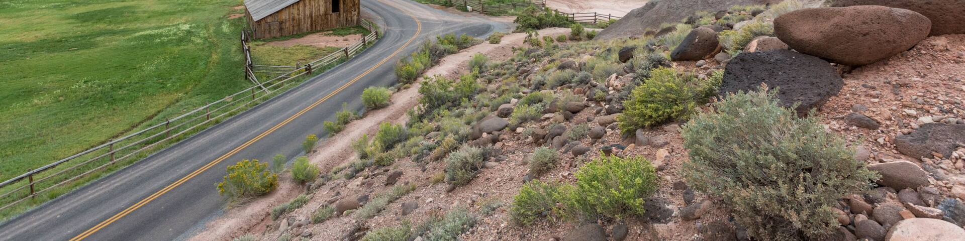 A rural landscape with a winding road, a wooden barn, and red rock formations in the background.