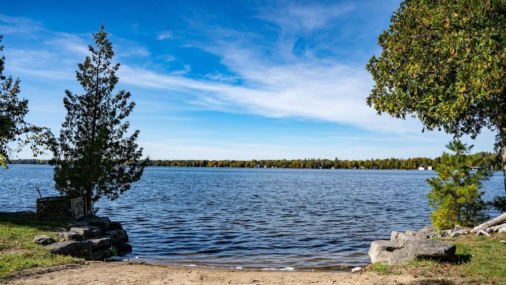 A lake with a sandy shore, trees, and a distant shoreline.