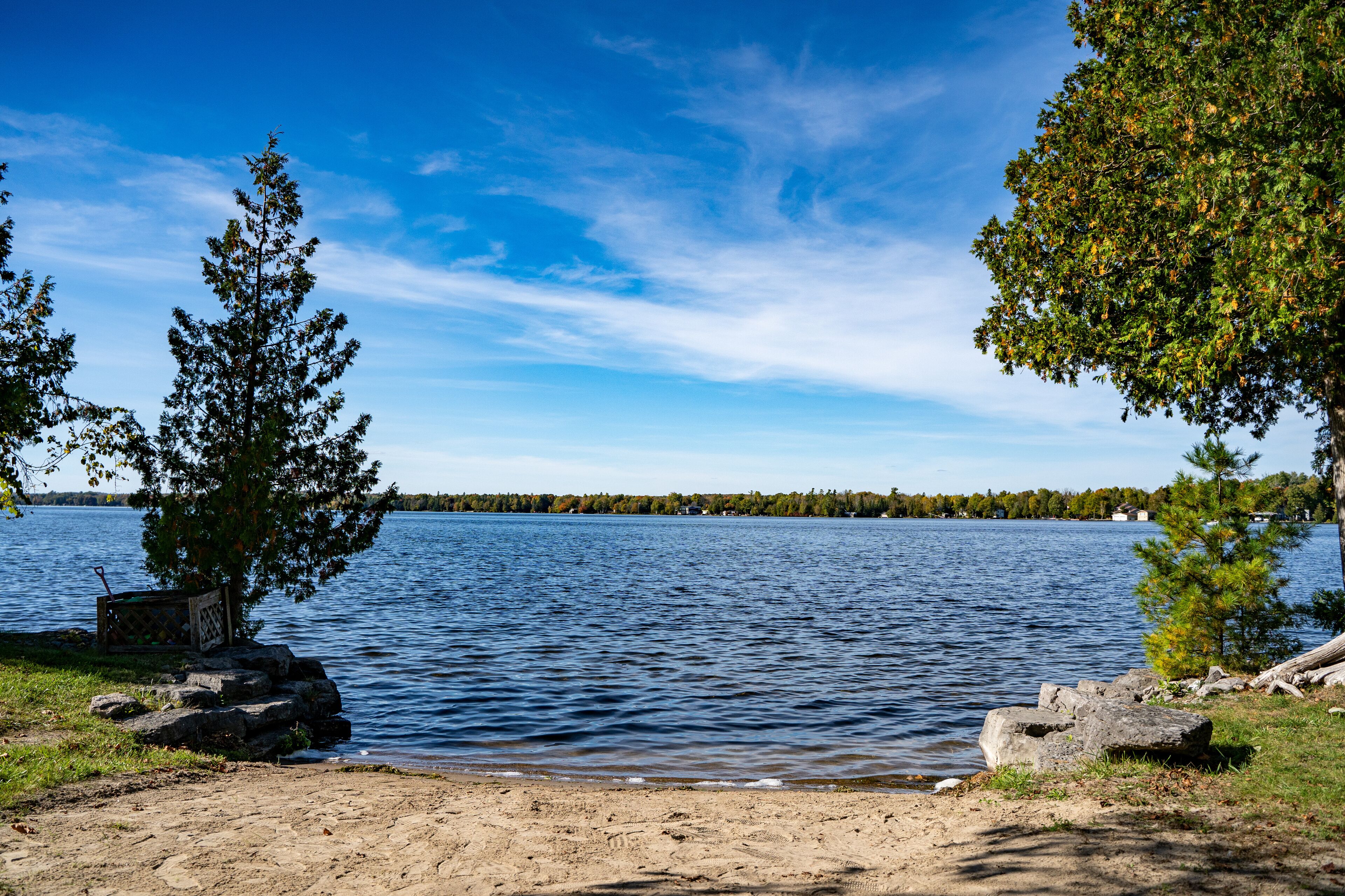 A lake with a sandy shore, trees, and a distant shoreline.