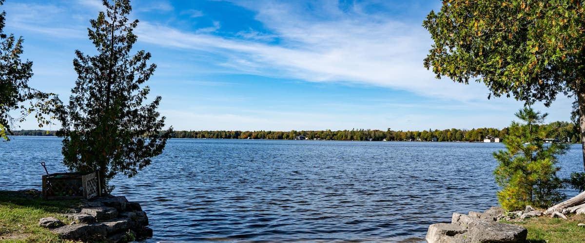 A lake with a sandy shore, trees, and a distant shoreline.