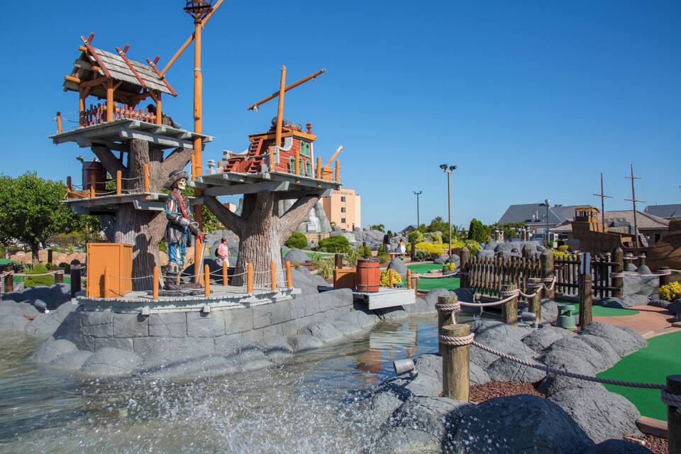 A pirate-themed water park with wooden play structures, a small waterfall, and a green pathway.