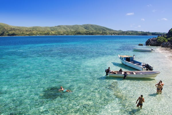 Une plage tropicale avec une eau turquoise et limpide, des bateaux et des gens qui profitent de la mer.