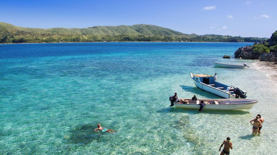A tropical beach with clear turquoise water, boats, and people enjoying the water.
