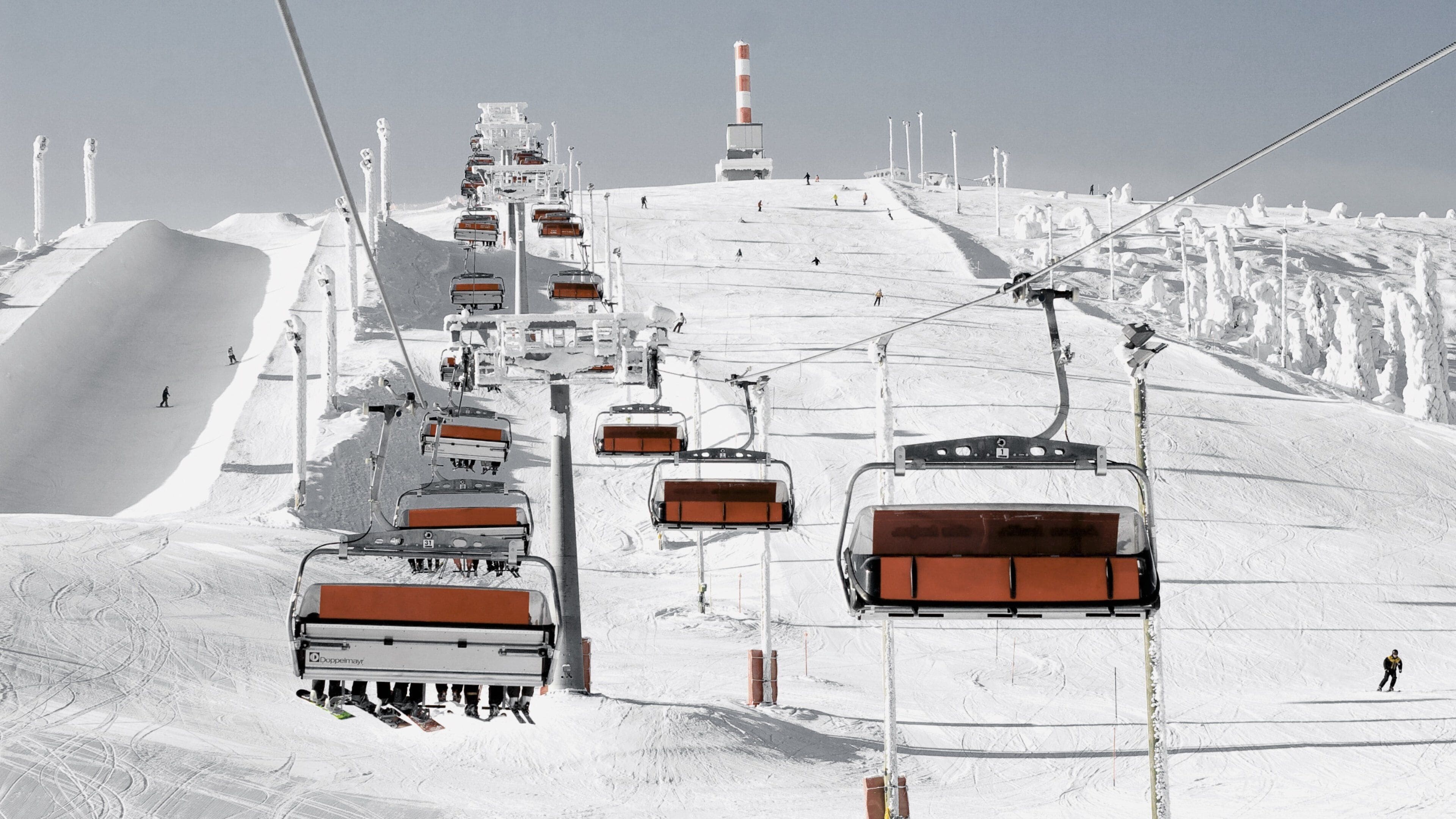 A ski lift with chairs ascending a snowy slope.