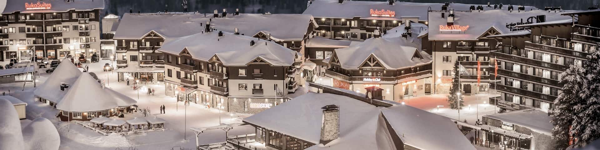 A snow-covered resort with multiple buildings, including Ruka Suites and Ruka Village, and a ski slope in the foreground.