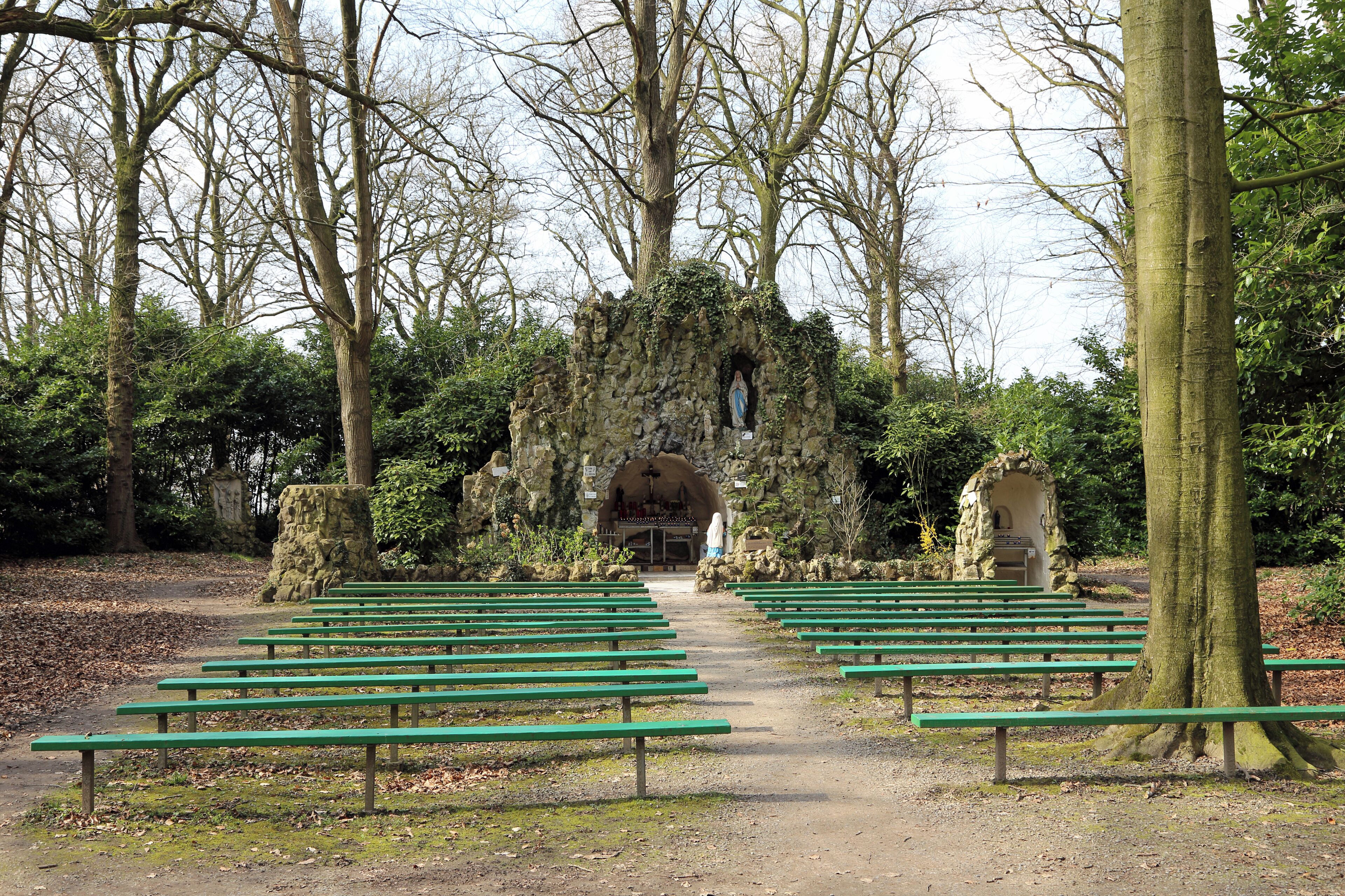 A pathway lined with green benches leading to a stone archway with a statue.