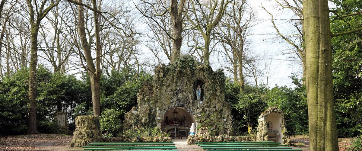 A pathway lined with green benches leading to a stone archway with a statue.