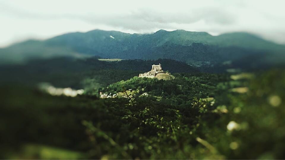 A castle on a hill surrounded by dense forest and mountains.