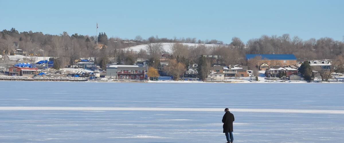 A person standing on a frozen lake with buildings and trees in the background.