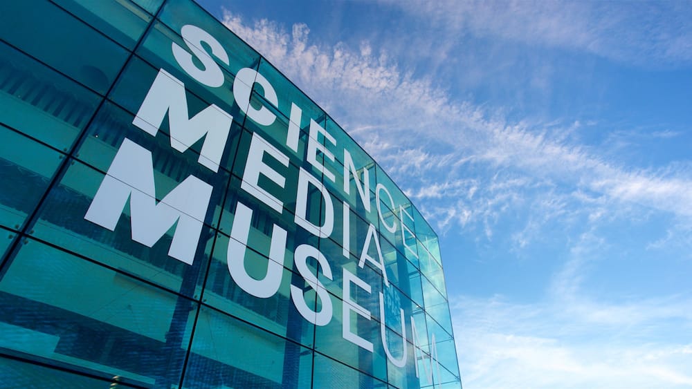 Un bâtiment moderne en verre dont la façade porte l’inscription « MUSÉE DES MÉDIAS SCIENTIFIQUES ».