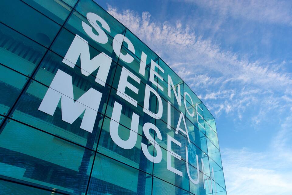 A modern glass building with the words "SCIENCE MEDIA MUSEUM" on its facade.