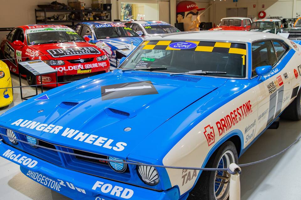 A blue and white Ford car with sponsor logos like Aunger Wheels and Holden in a car show.