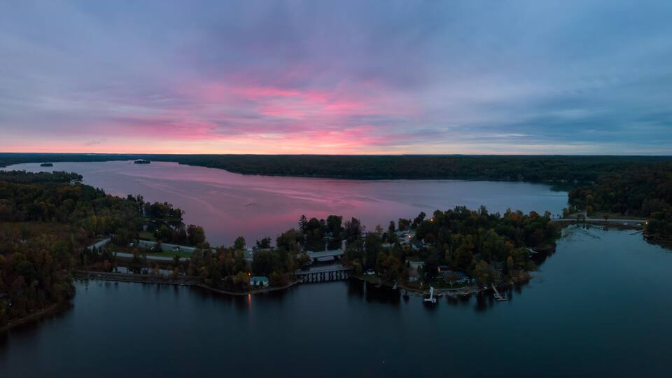 A lake surrounded by trees and houses at dusk.
